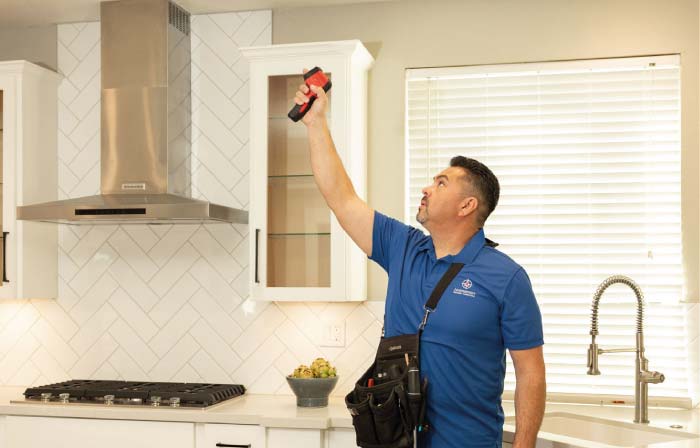 Certified home inspector using an infrared thermal imaging tool to evaluate a kitchen’s ventilation and structure, ensuring a technically sound and unbiased inspection for real estate transactions.